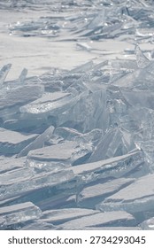 Sharp translucent ice plates, turquoise shards form dramatic frozen patterns on the surface of Lake Baikal with distant mountains in soft winter light