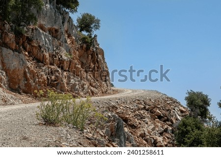 A sharp turn over the abyss. Dirt dusty road, steep rocky cliff, serpentine. The Mediterranean landscape is in the distance