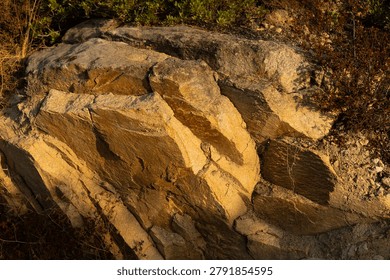 Sharp view of a massive rock formation showing layered geological structures, rough textures, and brown stone surfaces under bright warm sunlight.
