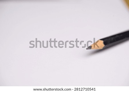 A sharpened black pencil tip resting on a blank white sheet of paper.