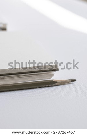 Sharpened pencil and notebook pages on white surface in studio close up. Minimal stationery, creative office, modern productivity, elegant branding, clean composition.