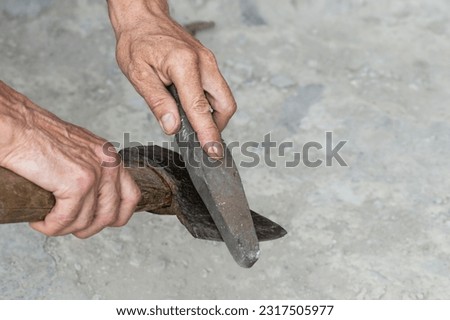 Sharpening the blade of an axe. A man sharpens the blade of an old rusty axe by hand with a grindstone.