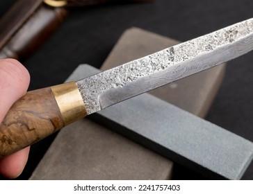 sharpening a Japanese knife with a whetstone. Beautiful wavy pattern of Damascus steel blade. high carbon steel blade. - Shutterstock ID 2241757403