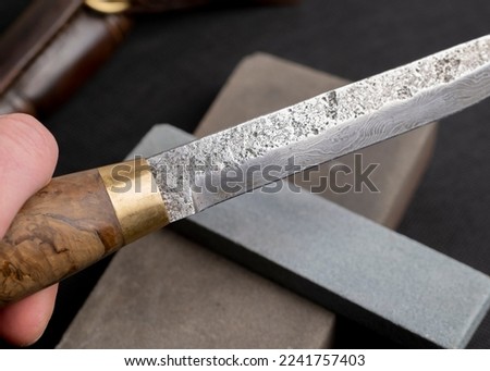 sharpening a Japanese knife with a whetstone. Beautiful wavy pattern of Damascus steel blade. high carbon steel blade.