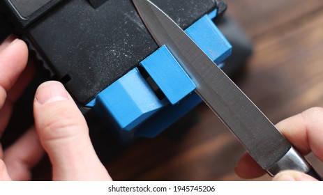 Sharpening a knife on an electric sharpener at home. The man's hand drives the knife blade between the blue sharpeners, dust flies on the machine.