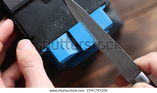 Sharpening a knife on an electric sharpener at\
home. The man\'s hand drives the knife blade between the blue\
sharpeners, dust flies on the\
machine.