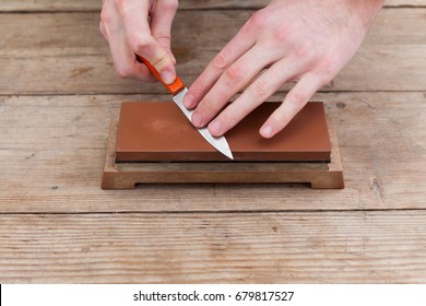 Sharpening the knife with a whetstone on a wooden background. Top view. - Shutterstock ID 679817527