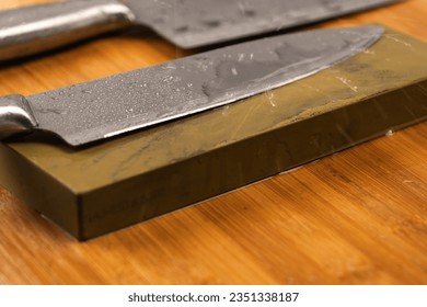 Sharpening knives with a Whetstone. Knife sharpening. Sharp knife and sharpening stone on a wooden cutting board.