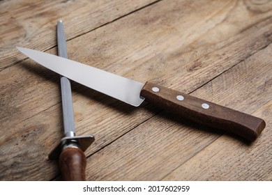 Sharpening steel and knife on wooden table, closeup