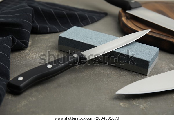 Sharpening stone\
and knives on grey table,\
closeup