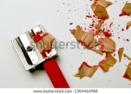Sharpening wooden red pencil in the sharpener and shavings. Isolated on white background.