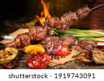 Shashlik or shish kebab prepared on barbecue grill over hot charcoal with grilled vegetables. Grilled pieces of pork meat on metal skewers.