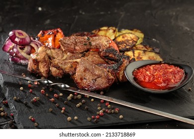 Shashlik Or Shish Kebab Prepared On Barbecue Grill Over Hot Charcoal With Grilled Vegetables And Hot Sauce. Close Up View.