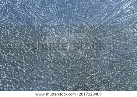 Shattered glass forms a starburst pattern against a soft blue background, highlighting fragility.