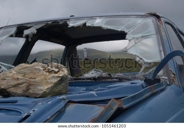Shattered windshield of a blue car frame in a\
hilly Irish landscape