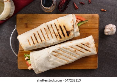 Shaurma chicken roll in a pita with fresh vegetables and cream sauce composition on wooden background