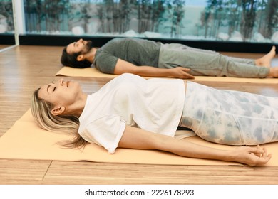 Shavasana. Man with woman wearing in sportswear practice yoga while lying down in savasana or corpse pose at wellness center - Shutterstock ID 2226178293