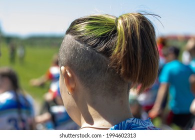 Shaved Whiskey And Green Hair. Modern Female Hairstyle. Hair Is Pulled Back In A Ponytail. Green Hair Dye. Partially Shaved Head. The Man Is Filmed From The Back Of His Head.