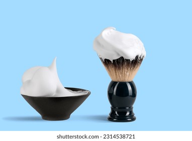Shaving brush with raccoon fur and shaving foam in ceramic bowl on blue background.