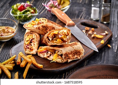 Shawarma chicken roll in a pita with fresh vegetables, cream sauce and french fries on wooden background. Selective focus