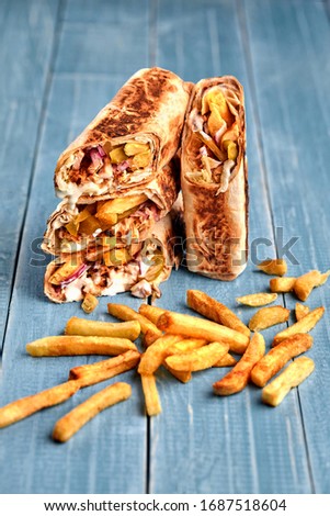 Shawarma chicken roll in a pita with fresh vegetables, cream sauce and french fries on wooden background. Selective focus Stock photo © 