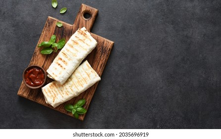 Shawarma with meat and vegetables on a wooden board on a black background, top view.