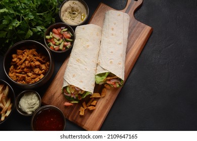 Shawarma Rolled Sandwich with Sauce and vegetables, Arab Traditional Food. Shawarma Doner kebab wrap with chicken, fries and pickles. Israeli Traditional homemade Shawarma on wooden cutting board.
