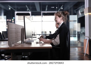 She adjusts the cursor mid task, jacket slung over her shoulders, the beige divider and black desks melting into the moody dusk interior in a bright modern coworking office.