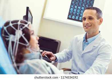 She is so brave. Selective focus on a cheerful lab worker grinning broadly while looking at a little girl undergoing electroencephalograph analysis.