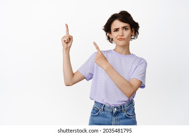 She doesnt like it. Skeptical brunette girl student frowning, pointing at upper left corner and sulking doubtful, disbelief, dislike smth, negative bad feedback, white background.