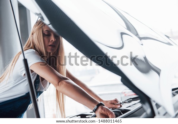 She knows what to do. On the\
lovely job. Car addicted woman repairs black automobile\
indoors.