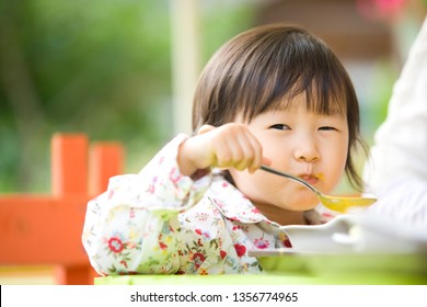 She Is A Lovely Child Sitting Next To Her Mom And Eating Soup.