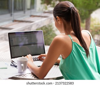 She makes technology work for her. Rearview shot of a young woman working on her laptop outside.