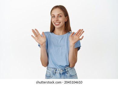 She Is Not Involved. Smiling Blond Girl Raising Empty Hands Up And Looking Careless, Nothing To Say, Being Unaware And Clueless, Standing In T-shirt Against White Background