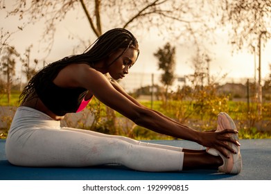 She Is Sitting On The Floor Streching Her Legs With Her Hands On Her Feet.