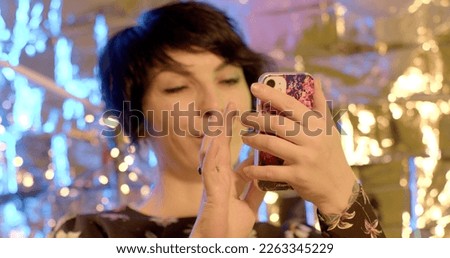 She uses the phone in her hands against the backdrop of light reflections. Check notifications and messengers at the party. Focus on the screen, press the finger, scroll.