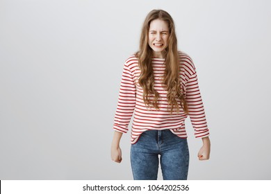She will grow and revenge all bullies and bad guys. Portrait of angry weak european teenager clenching teeth not to cry, being furious and offended, standing over gray background with ready fists
