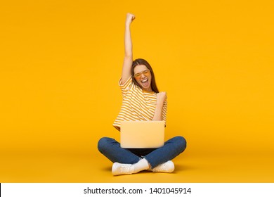 She is a winner! Excited young female with laptop isolated on yellow background - Shutterstock ID 1401045914