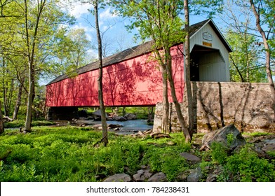 Sheard's Mill historic covered bridge, in Bucks County, Pennsylvania, spans a small stream.  This photo was taken in the summer when the surrounding landscape was lush and green with blue sky.