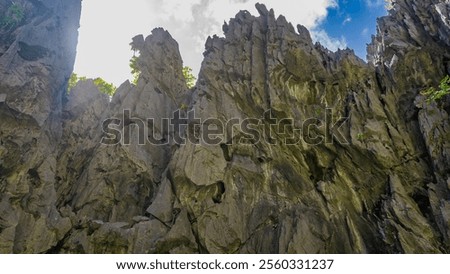 Sheer karst cliffs against a background of blue sky and clouds. Steep furrowed slopes, green vegetation, sharp peaks. Bottom-up view. Philippines. Palawan.