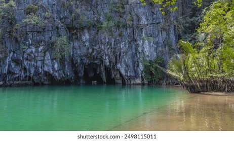 Sheer karst cliffs rise above the turquoise river. A boat with tourists floats into the dark entrance of the cave. Green tropical vegetation. An underground river. Philippines. Palawan.Puerto Princesa - Powered by Shutterstock