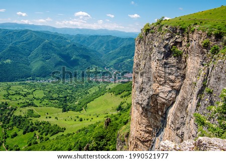 Sheer rock face, in the background green pastures and mountain ranges. Mountain landscape in the spring over the town of Teteven, Balkan Mountains (Stara Planina), Bulgaria.