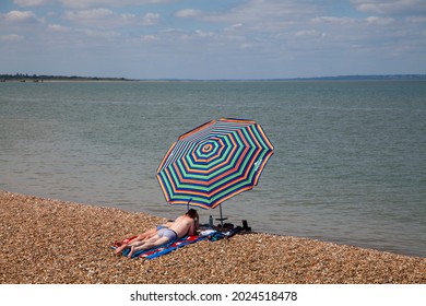 Sheerness UK - 07 03 2021: A Couple Sun Bathing On A Deserted Beach With Parasol