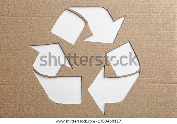 Sheet of cardboard with cutout recycling symbol on\
white background, top\
view