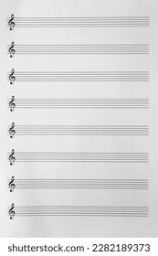 Sheet with empty staves for music notes and treble clef as background, top view