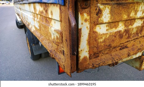 Sheet Metal Corrosion Of Body Of An Old Truck. Rusty Surface, Background And Damaged Texture From Road Salt And Reagents. Protection And Professional Paintwork Concept. Dirty Cargo Bed.