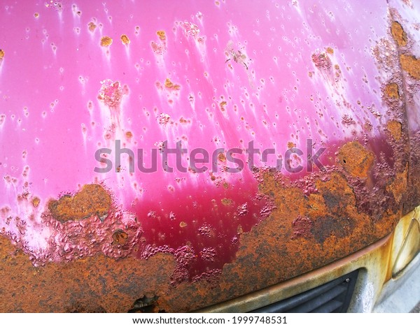 Sheet metal corrosion of bonnet of old red
wine-colored car. Rusty messy surface. Damaged grunge dirty texture
from road salt. Rust background. Protecting the automobile concept.
Paint work. Insurance