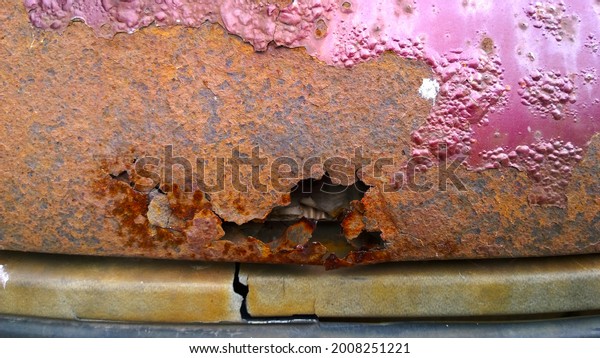 Sheet metal corrosion of old red car. Rusty messy\
surface. Damaged grunge dirty texture from road salt. Rust\
background. Protecting the automobile concept. Coat. Copy space.\
Paint and repair. Hole.