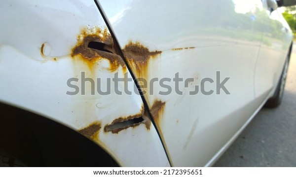 Sheet metal corrosion of old white car. Rusty\
surface, background and damaged corroded texture, hole. How to\
remove steel rust from vehicle. Protection and paint auto concept.\
Car accident. Insurance.