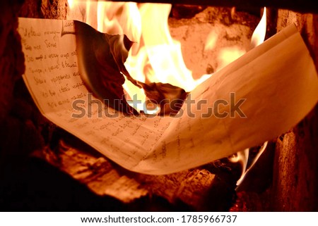 a sheet of paper is burning in the fireplace, a bright flame and firewood.  the letter burns in the fire